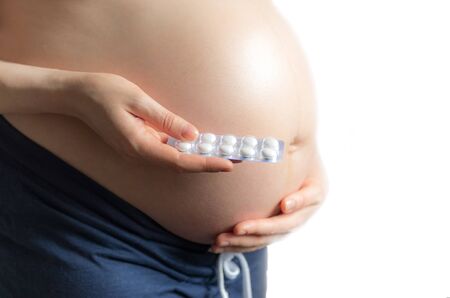 pregnant girl holding pills on the background of pregnant belly, the concept of taking drugs and...