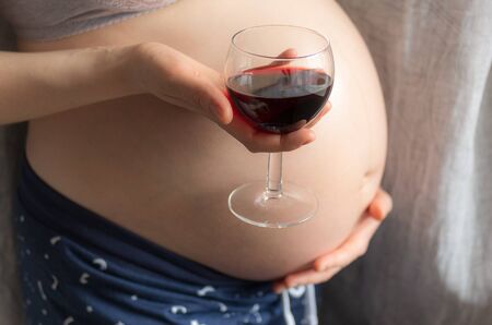 pregnant woman holding a glass of wine on background of the pregnant belly, the concept of alcohol intake during pregnancyの写真素材