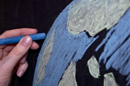 hand with chalk drawing on the Board of the planet earth, chalk drawing