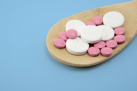 multi-colored tablets in a wooden spoon on a blue background isolated, blank, mock up, copy space