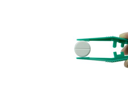 green plastic tweezers in hand holding white round tablet isolated on white background