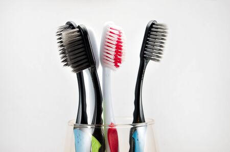 multi-colored toothbrushes in a glass on a light background