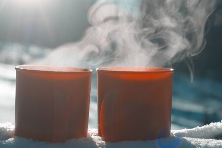 red mugs with a hot drink soar in the cold, mugs in the snow on a Sunny frosty day, picnic in the winter campaignの写真素材