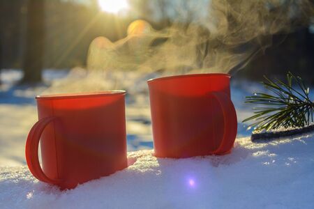 red mugs with a hot drink of coffee or tea in the snow, a walk in the winter forest, a picnic in nature, winter moodの写真素材