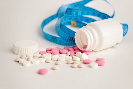 blister with tablets with measuring tape, the concept of taking drugs for weight loss and maintain the figure, the harm of supplements for weight loss,  on white backgroundの写真素材