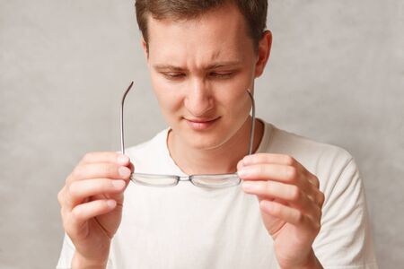 the young man holds glasses with diopter lenses and looks through them, the problem of myopia,...