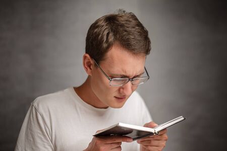 the young man holds glasses with diopter lenses and looking at the book, the problem of myopia,...
