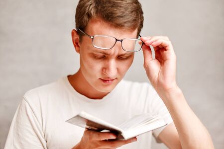 the young man holds glasses with diopter lenses and looking at the book, the problem of myopia,...