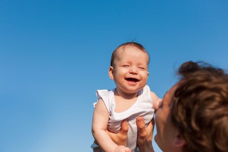 little baby in father's arms against blue sky , father's day, fatherhood, happy babyの写真素材