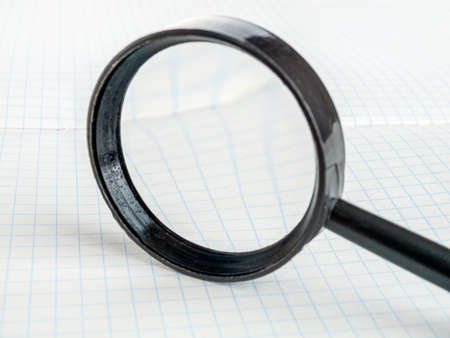 Magnifying glass on the background of a notebook in a cage, reading small text, selective focusの写真素材