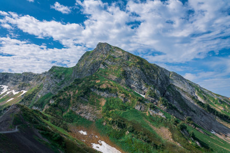 picturesque beautiful panorama view of the mountain gorge mountain ranges covered with greenery forests and snow against the background of the blue sky wide angleの写真素材