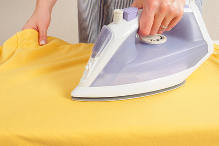 Girl ironing clothes with an iron on an ironing board selective focus close-upの写真素材