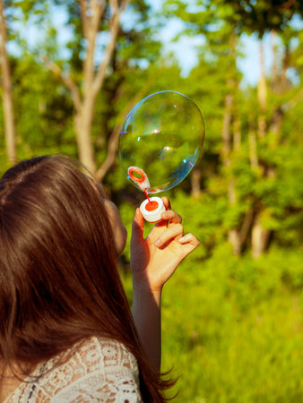 A young girl blows soap bubbles on a sunny summer day against the background of a park close-upの写真素材