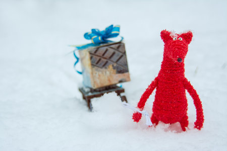winter holiday background red toy fox carrying a toy sled and a gift against the backdrop of snowy weather and snow, close-upの写真素材