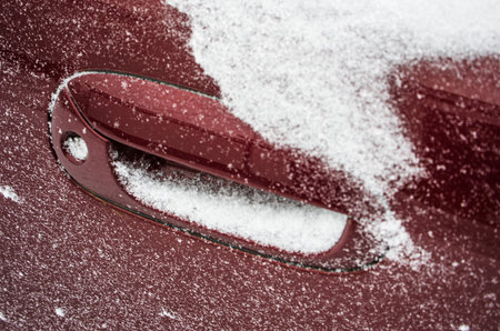 fallen snow covering the car, frozen car doors and windows, winter road, snow piles and ice on the roads, close-upの写真素材