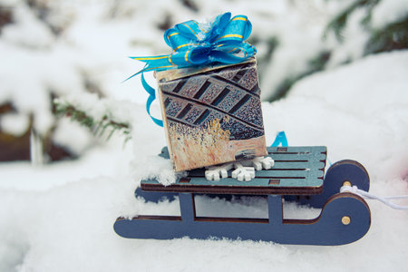 winter holiday background with a toy sled carrying a gift against the backdrop of snowy weather and snow, close-upの写真素材