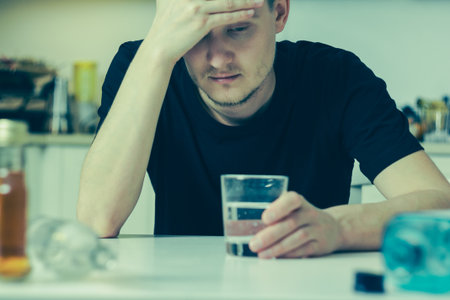 A man suffers from a hangover at the table: he sits with his head down, holding his forehead, a...