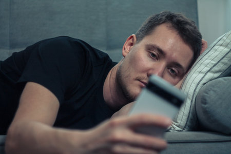 A man is procrastinating: sitting with a phone in his hands, relaxed position, concentrated gaze on...