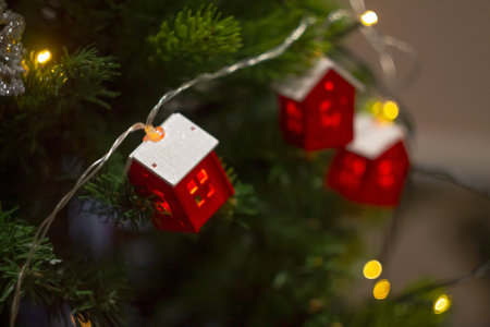 A Christmas garland in the form of houses, sparkling with lights on the tree, creates a cozy atmosphere and a magical holiday mood.の写真素材