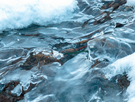 Winter landscape: a frozen stream covered with ice and snow creates an atmosphere of calm and beauty of the cold season.の写真素材