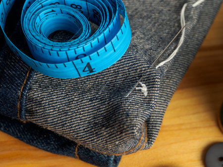 Close-up of a threaded needle and measuring tape against a background of fabrics, symbolizing the...