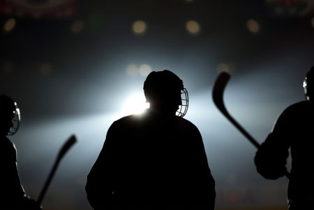 A dramatic silhouette of a hockey goalie in the center of an ice rink with blurred lights and players in the backgroundの素材