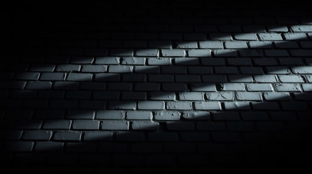 A dark, textured brick wall with dramatic shadows and light patterns.の素材