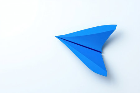 A single blue paper airplane resting on a white surface.の素材