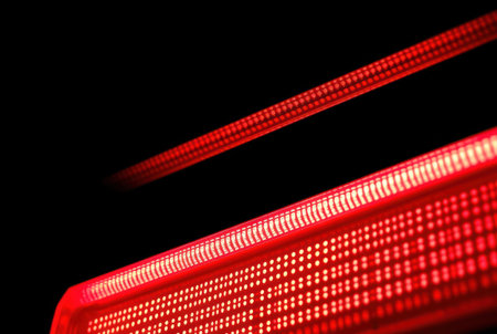 Close-up image of a red LED light bar reflecting intensely on a dark surface.の素材