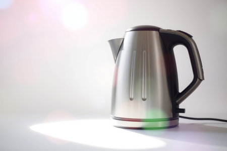 A glaming stainless steel electric kettle sits on a surface with light reflection.の素材