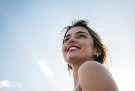 A beautiful young woman gazing upwards at a bright blue sky.の素材