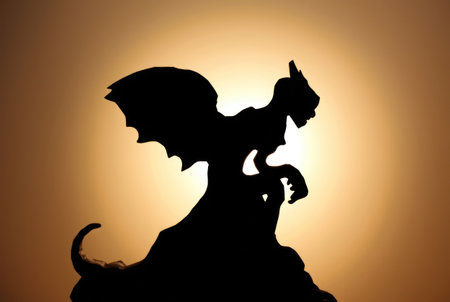 A dramatic silhouette of a dragon resting on a rocky outcrop during sunset.の素材