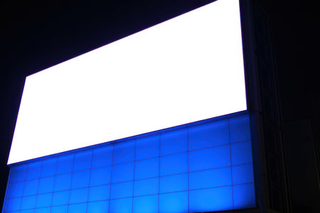 Large illuminated electronic display dominates the night cityscape with blue and white light.の素材