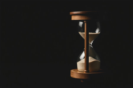A vintage hourglass filled with sand rests on a dark wooden base.の素材