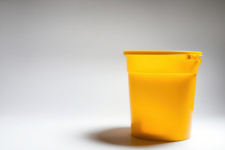 A solitary yellow plastic bucket resting on a white surface in shadow.の素材