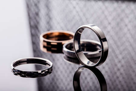 Group of beautiful jewelry rings in gold, silver, platinum closeup on a table with reflection and with a fashionable gray backgroundの写真素材