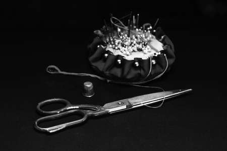Needle bed, thimble, scissors, needle and thread on black fabric background. Black-white.の写真素材
