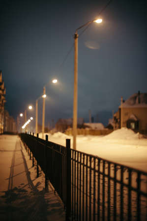 The fence is removed for a distance along the road. Lantern posts go to blur along the fence. Night.の写真素材