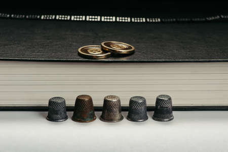 Thimbles are arranged in a row on the background pages of the book. The buttons on the book. Conceptual photography.の写真素材