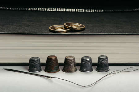Old Thimbles and a needle and thread on a background of book pages. The buttons on the book. Conceptual photography.の写真素材