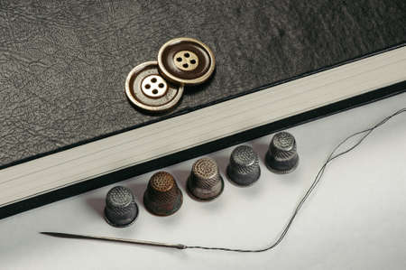 Gold Buttons on the book. Old Thimbles and a needle and thread on a background of book pages. Conceptual photography.の写真素材