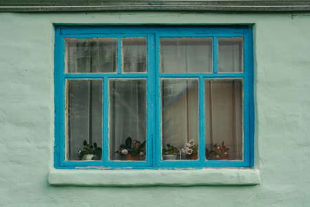 Blue wooden window of an old private house, whose walls are painted in light green color. The old building. Plastered walls.の写真素材