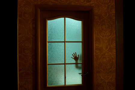 The child's hand through the glass door in the apartment. Green light from the room. Fear.の写真素材