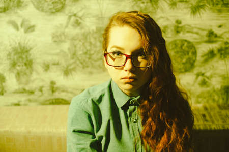 Portrait of a red-haired girl in a room with green lighting. Hairstyle - curly hair on one side....