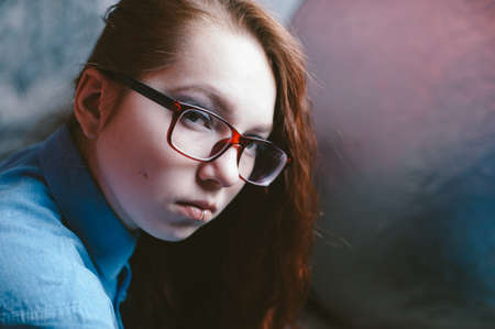 Artistic portrait of a red-haired girl in red glasses in a semi-half. Piercing in the lip.の写真素材