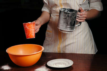 The girl is holding a glass of flour and a flour sieve. Black background. Concept.の写真素材