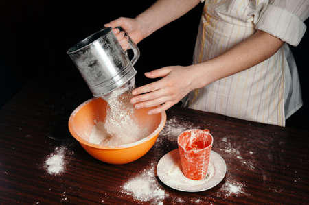 The girl sifts the flour in a steel sieve. Bright kitchen items.の写真素材