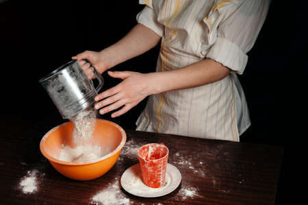 The girl sifts the flour in a steel sieve. Bright kitchen items.の写真素材