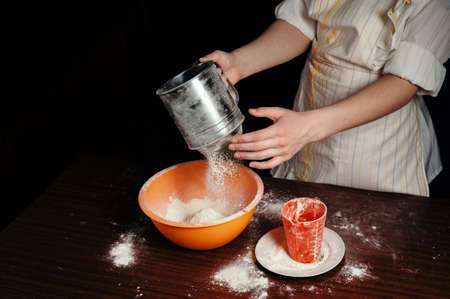 The girl sifts the flour in a steel sieve. Bright kitchen items.の写真素材