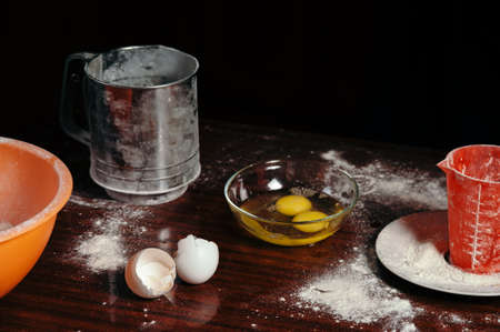 Scattered flour on a wooden table, broken eggs in a glass bowl, eggshell.の写真素材